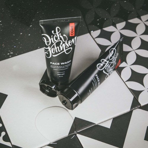 Two black tubes of Dick Johnson face wash placed on black and white geometric tiles.