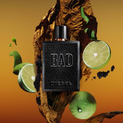 A Diesel perfume bottle labeled 'BAD' surrounded by limes, black particles, and a textured background.