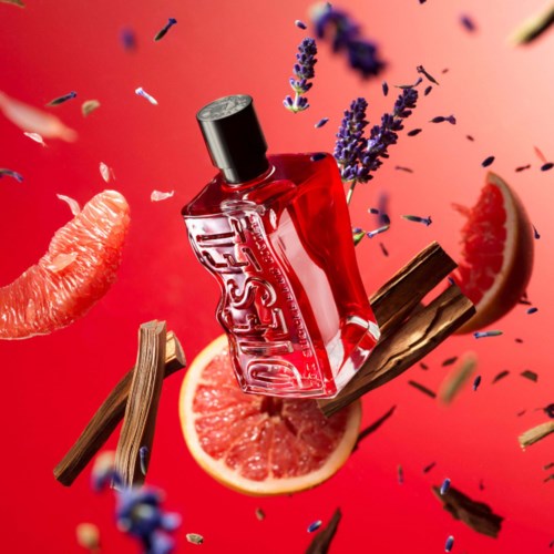 A glass perfume bottle with lavender, grapefruit, and chocolate pieces around it, mid-air with scattered ingredients.