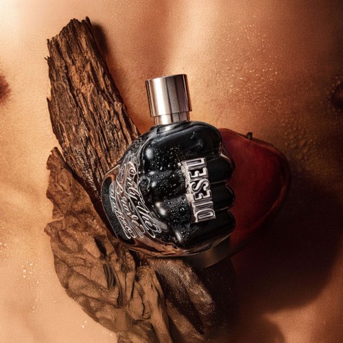 A Diesel perfume bottle lies on wooden pieces in warm lighting, creating a moody, rustic scene.