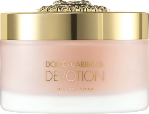 Een roze lichaamscrèmepot met een gouden deksel en een doorzichtige decoratieve bovenkant, gelabeld Dolce & Gabbana Devotion.