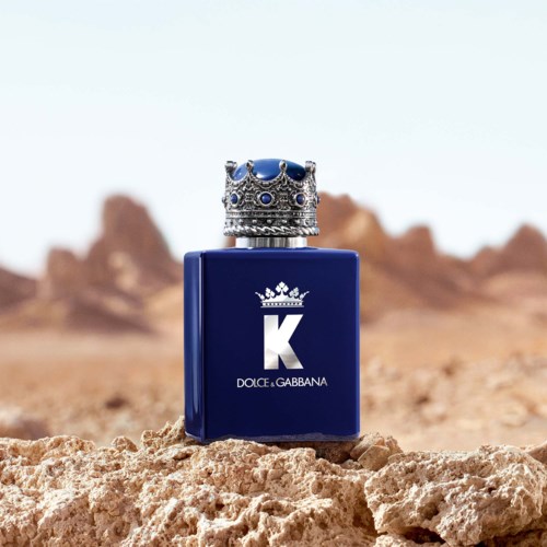 Een blauw parfumflesje met een kroon-top, geplaatst op woestijnrotsen met een ver rotsachtig landschap op de achtergrond.
