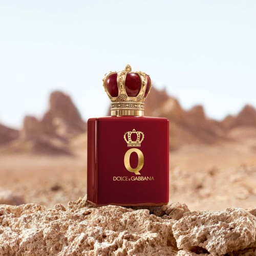 Een rood parfumflesje met een gouden kroon erop, geplaatst op een rotsachtige woestijnachtergrond.