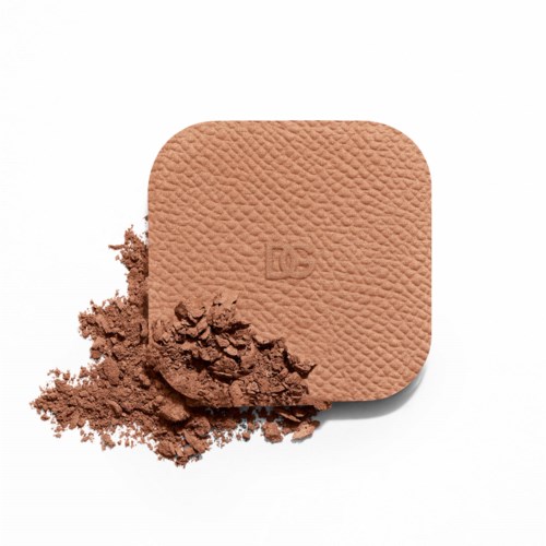 A pressed powder blush with some powder spilled beside it on a white background.