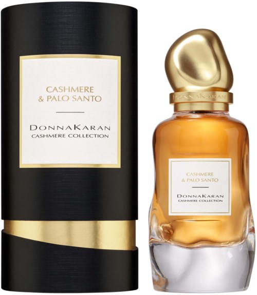 Een parfummerkfles met een gouden dop en etiket, naast een lange zwarte en goudkleurige cilindrische doos. Beide van Cashmere & Palo Santo.