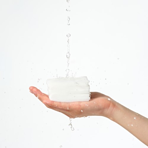 Een hand houdt een stapel witte zeep met druppels water die vallen.