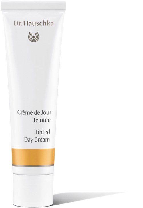 En vit tub med tonad dagkräm, med ett guldband längst ner, märkt "Dr. Hauschka Tint Day Cream".