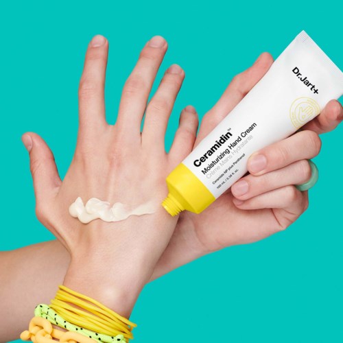 Een hand brengt crème aan van een tube met de tekst 'Ceramidien' op de achterkant van een andere hand, met kleurrijke armbanden aan de pols.