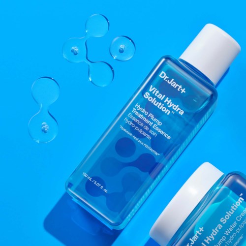 Een blauwe flesje met label 'Dr. Jart+ Vital Hydra Solution' en witte dop, omgeven door watermoleculen.