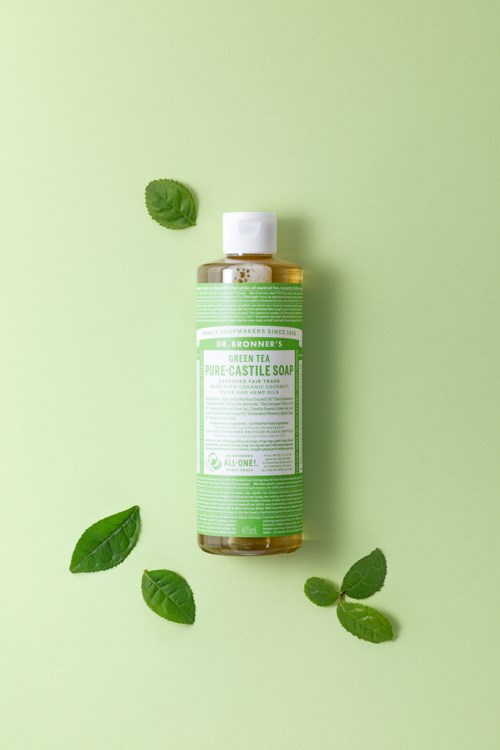 Een groene fles tea tree castile-zeep met vier theeënten eromheen op een groene achtergrond.