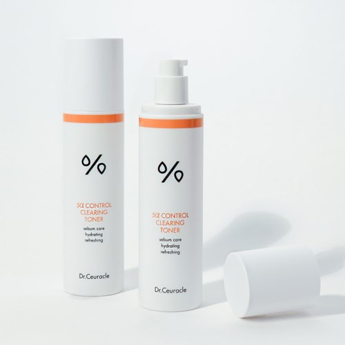 Twee witte flesjes huidverzorgingstoner met oranje details, één met pomp en de andere met deksel, op een witte achtergrond.
