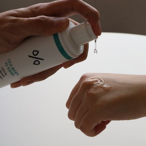 Iemand smeert lotion of crème op de hand, met een druppel die uit de fles op de huid valt.