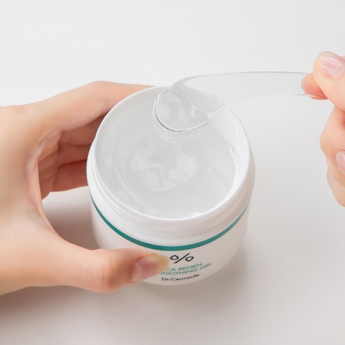 Eine Hand hält ein Cremetopf, während ein Löffel etwas Creme herausnimmt.