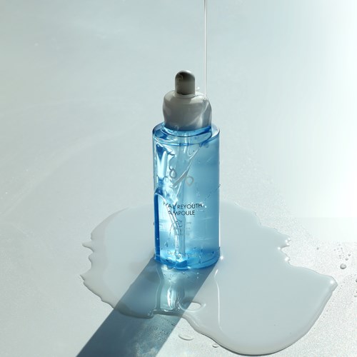 Een blauwe huidverzorgingsfles met pipettendop, die wat vloeistof morst op een witte ondergrond.