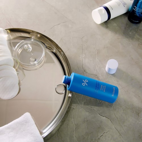 Cosmeticaflessen, watpads, een handdoek en een dienblad op een badkamer oppervlak.
