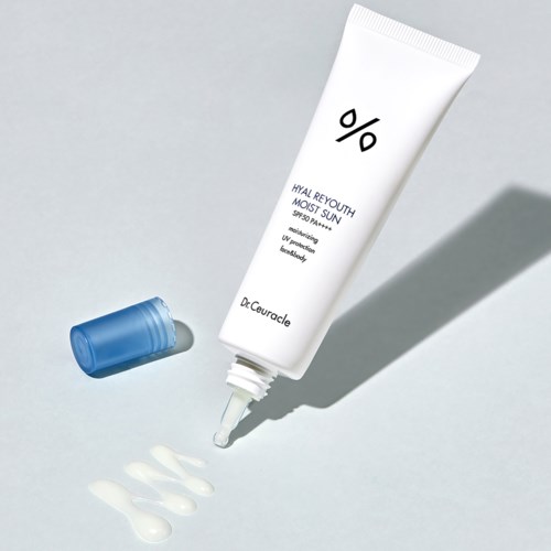 A white tube of sunscreen with a blue cap, showing drops and a spill on a light surface.