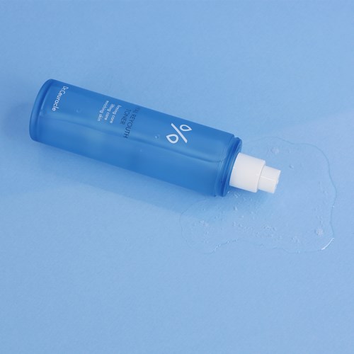 Een blauwe fles ligt op een blauwe ondergrond, met wat vloeistof eromheen gemorst en een witte spraykop bovenaan.