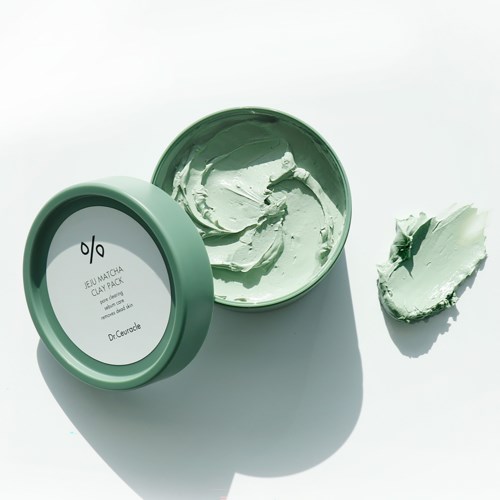 Groene thee matcha kleipack in een ronde container, met wat klei ernaast op een witte ondergrond.