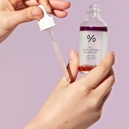 Iemand houdt een glazen fles met paarse vloeistof en een pipet, brengt olie serum aan op hand.