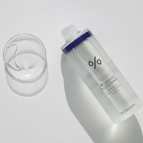 Een heldere fles toner gekanteld naast een glas met vloeistof, op een witte achtergrond.