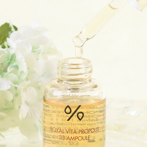 Een pipet druppelt vloeistof in een klein glazen flesje met label 'Royal Vita Propolis 33 Ampoule'.