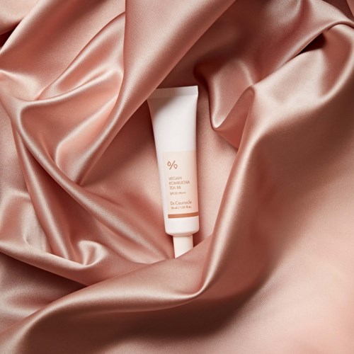 Vegan skincare product in a white tube on shiny pink silk fabric.