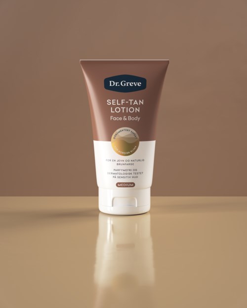 En brun og hvit tube merket 'Dr. Greve Self-Tan Lotion' står oppreist på en beige overflate mot en enkel bakgrunn.