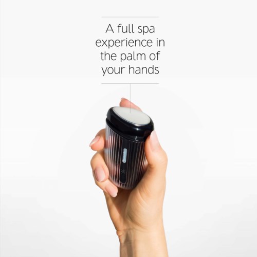 En hand som håller en liten svart massager med rund vit huvud, som marknadsför en spa-upplevelse i handflatan.