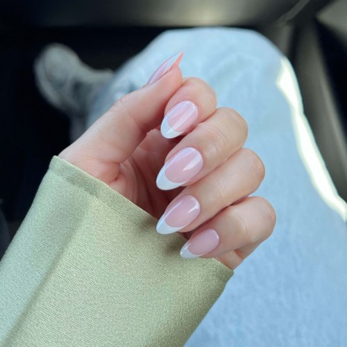 A hand with well-manicured nails shows French tips and a green sleeve, resting on a person's knee.
