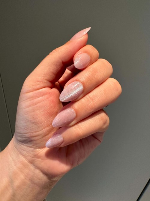 A hand with long pink and shiny nails is in focus against a plain background.