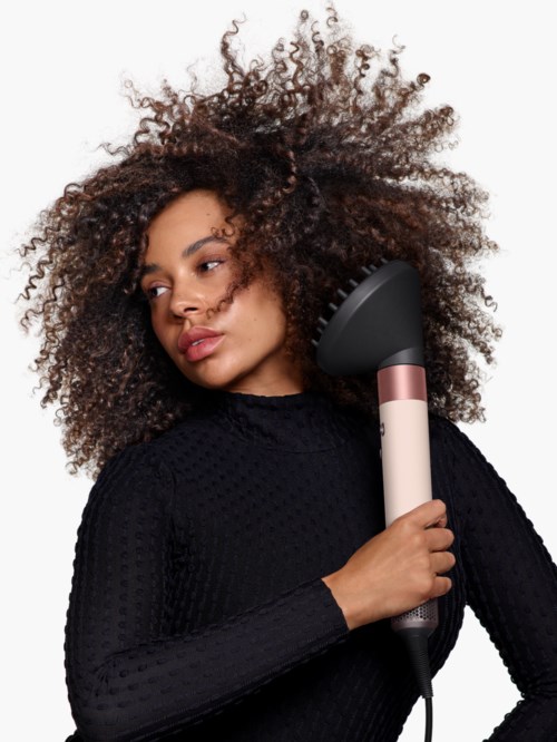A woman with large curly hair holding a black and white hair dryer.