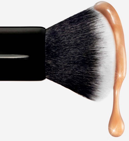 Makeupborste applicerar foundation, med en droppe foundation bredvid. Rent och enkelt design.