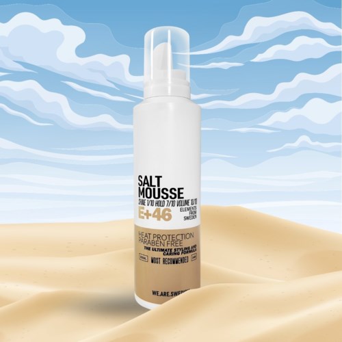 Eine weiße Sprühflasche mit 'Salt Mousse'-Aufschrift steht auf Sand vor Himmel mit Wolken.
