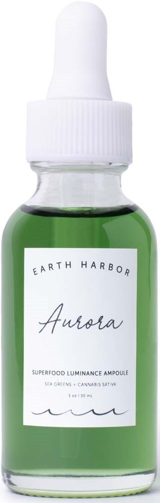 A small green bottle with a dropper cap labeled 'Earth Harbor Aurora' for skincare. The label mentions 'Superfood Luminance Ampoule.'