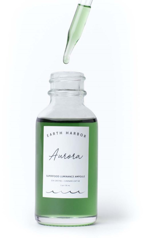 A bottle with a dropper, containing green liquid, labeled Earth Harbor Aurora, a skincare superfood luminous ampoule.