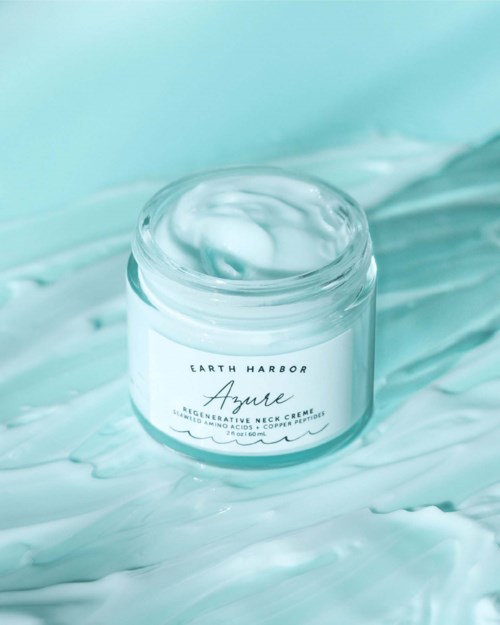 A white jar of Earth Harbor Azurene reformative neck cream on a mint green background with cream spillage.