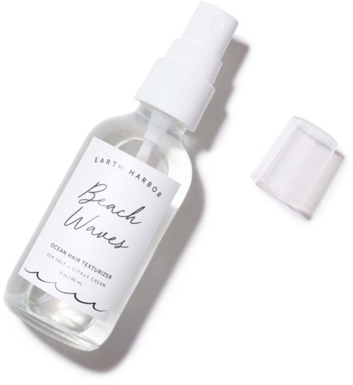 En genomskinlig sprayflaska märkt "Beach Waves" med vit lock och en separat spraymunstycke.