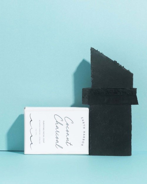 A white box and three black charcoal pieces on a light blue background. The box has text on it.