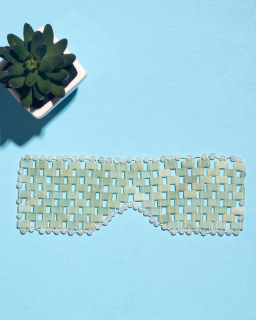 A woven eye mask made of beads, placed on a blue background, with a potted succulent nearby.