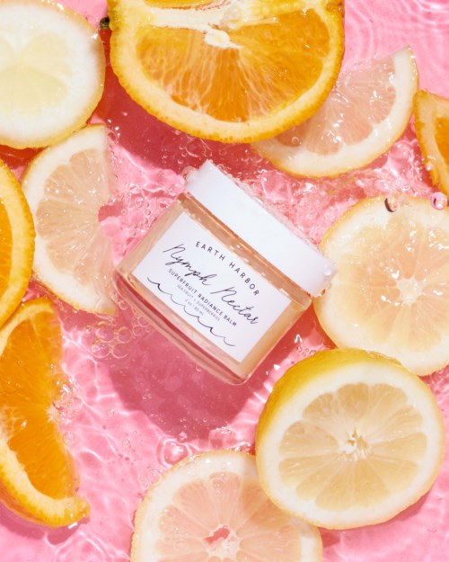 A jar of Earth Harbor lip balm surrounded by lemon and orange slices on a pink background.