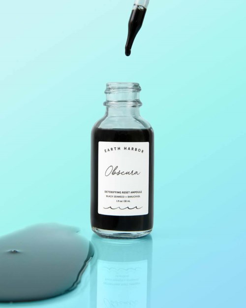 A small bottle with a dropper, labeled Earth Harbor, containing a dark liquid. A spill of the liquid is on the surface.
