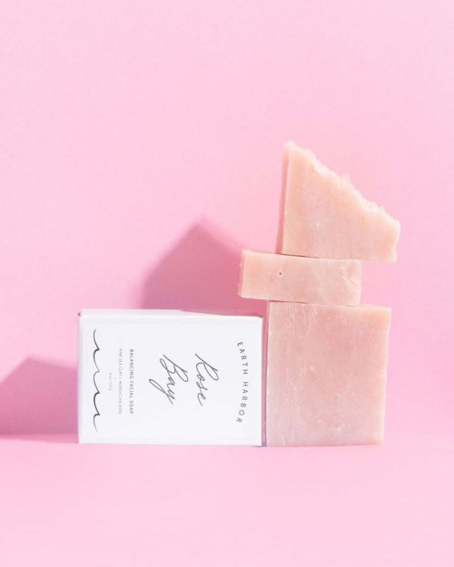 Pink soap bars stacked, with one triangle piece on top, against a pink background.