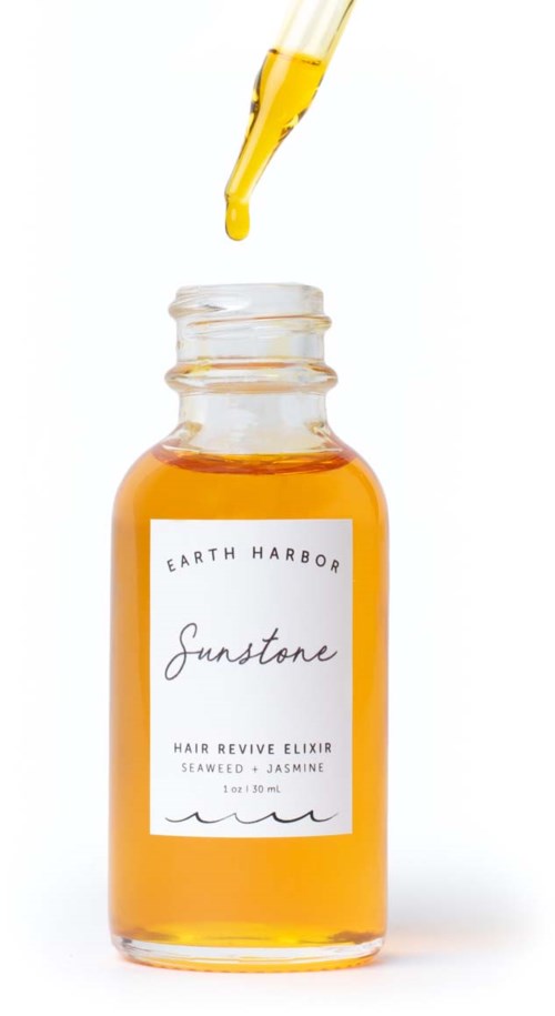 A small funnel drops yellow liquid into a jar labeled 'Sunstone Hair Revive Elixir' with seaweed and jasmine ingredients.