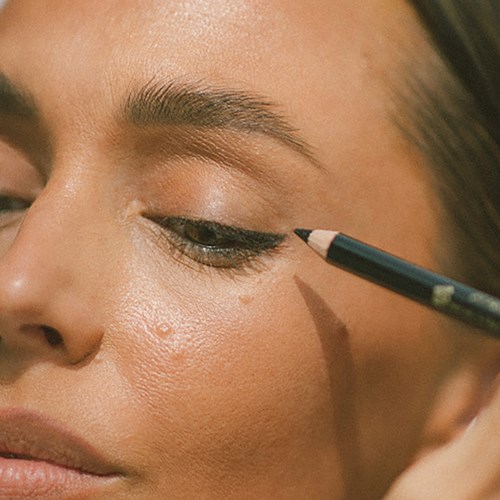 Eine Frau trägt Eyeliner mit einem Stift auf das Augenlid auf, konzentriert sich auf das Auge und die Augenbraue. Die Haut ist klar und strahlend.