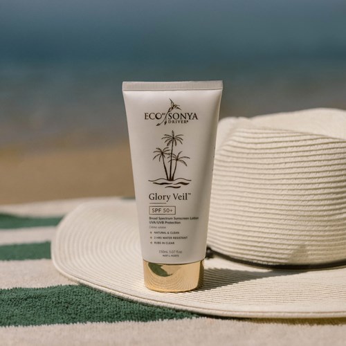 Een witte tube zonnebrandcrème met een palmboomlogo, op een strandhoedje naast de zee.