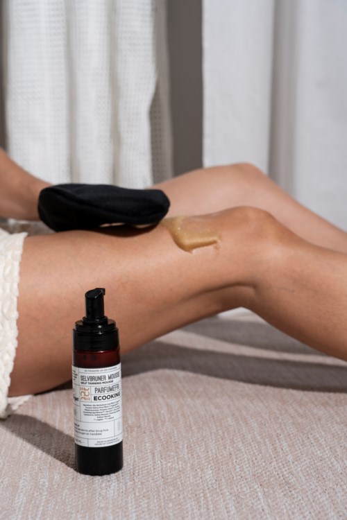 A person applying lotion or cream to their leg, with a pump bottle nearby, in a cozy setting.