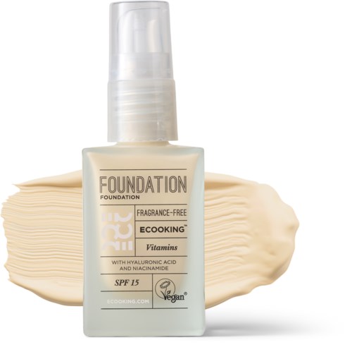 A bottle of fragrance-free foundation with vitamins, SPF 15, vegan label, and a cream streak background.