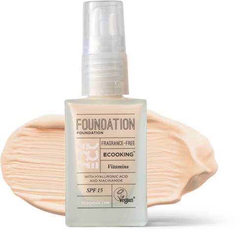 Vegan foundation bottle with SPF 15, hyaluronic acid, niacinamide, and fragrance-free. Cream is spread behind it.