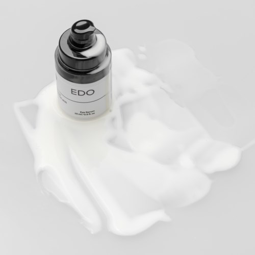 Eine Flasche mit der Beschriftung 'EDO' auf weißer Creme oder Lotion mit etwas verschüttetem Produkt darum.