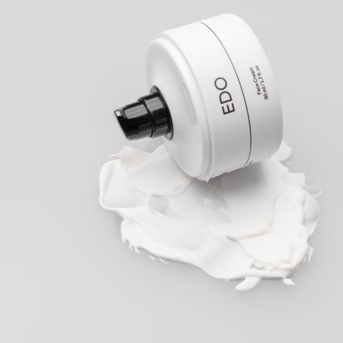 Ein weißer Tube mit schwarzer Spitze, beschriftet 'EDO', tropft Creme oder Lotion auf eine graue Oberfläche.
